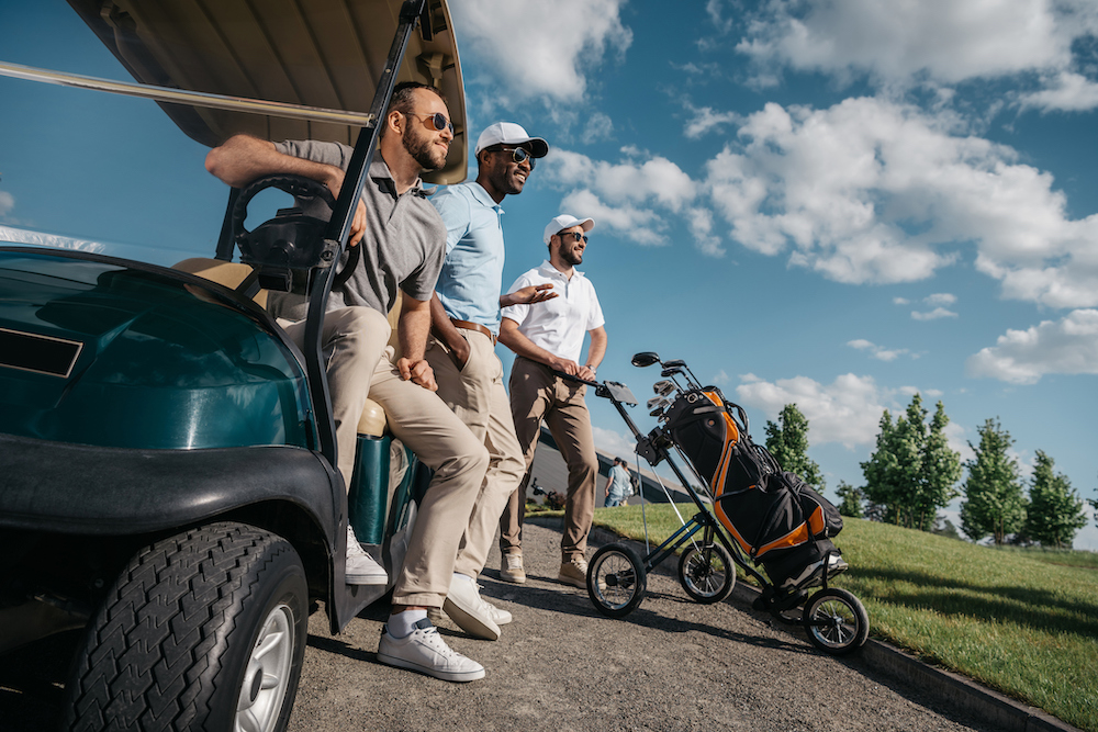 group of smiling friends standing near golf cart and looking away