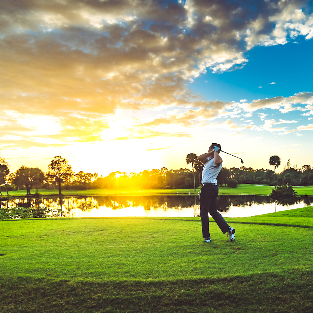 Man on a beautiful scenic sunset golf course swings a golf club
